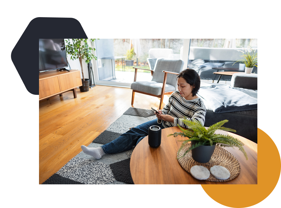 A woman sitting on the floor using a handheld device and a voice activated virtual assistant.